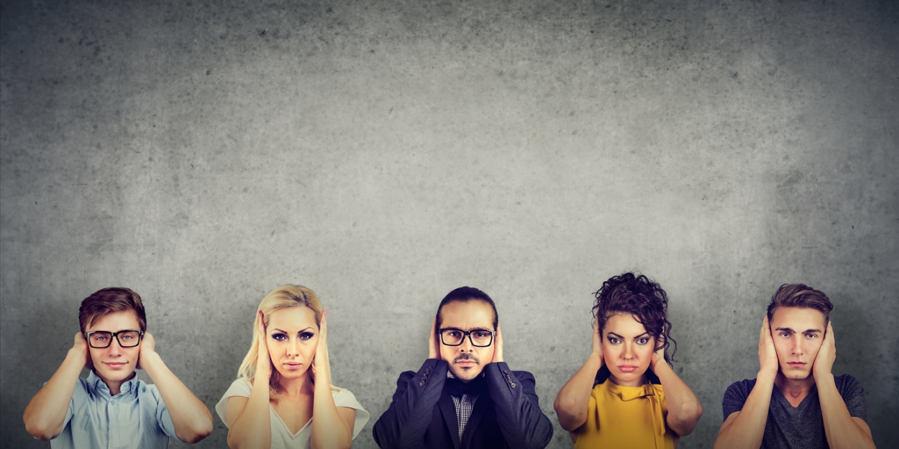 A line up of two women and three men looking stern, each with their hands covering their ears. The background is grey.