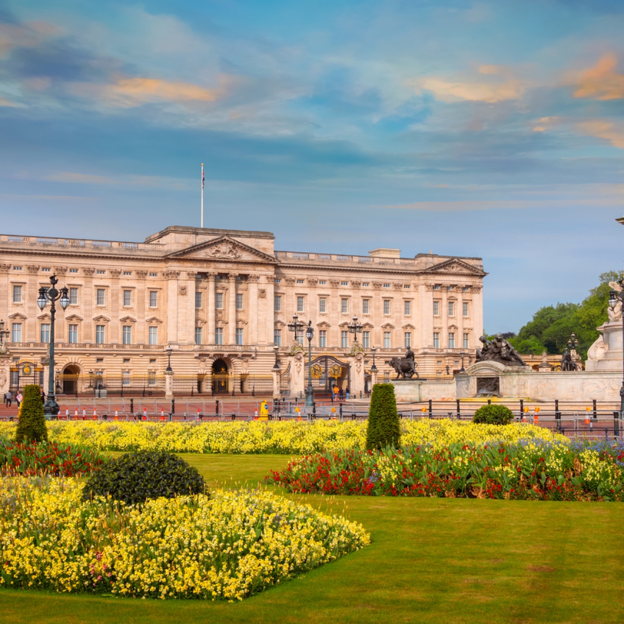 Buckingham Palace against a blue sky. There is green grass and colourful flowers in the foreground.