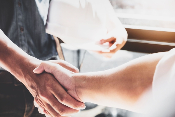 Two unseen figures shake hands, one holding a hard hat and wearing dark clothes