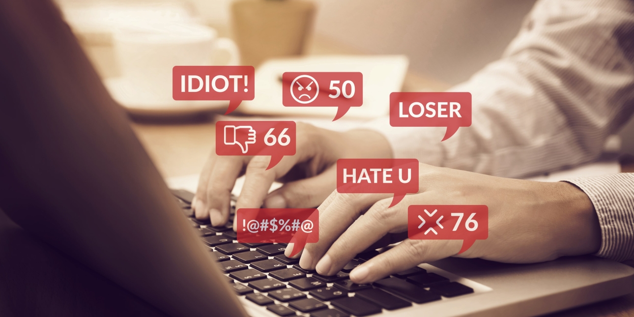 Hands typing at keyboard with speech bubbles suggesting words such as idiot, hate and loser