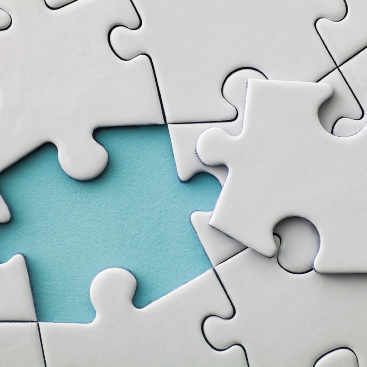 Close up of a plain off-white jigsaw puzzle. The final piece is placed on top of the others, with a turquoise background showing where the space where is to be inserted