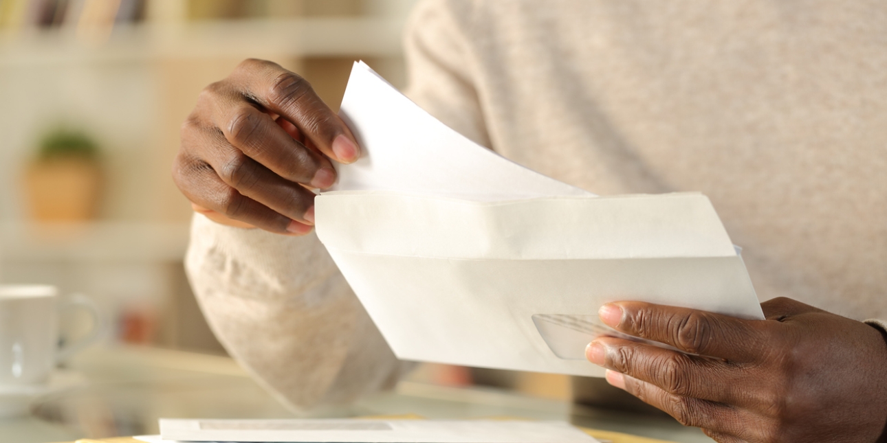 A hand pulling paper from an envelope. There are more unopened envelopes on the table.