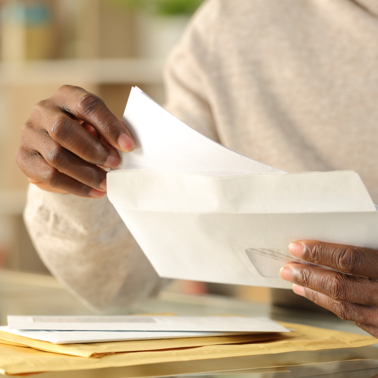 A hand pulling paper from an envelope. There are more unopened envelopes on the table.