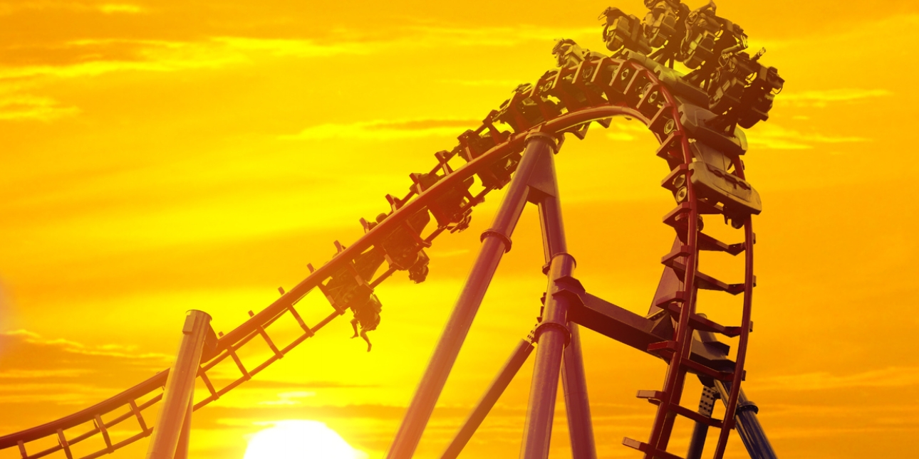 A rollercoaster begins its descent, turning occupants of the cars upside down. The sun sets in the background turning the sky yellow.