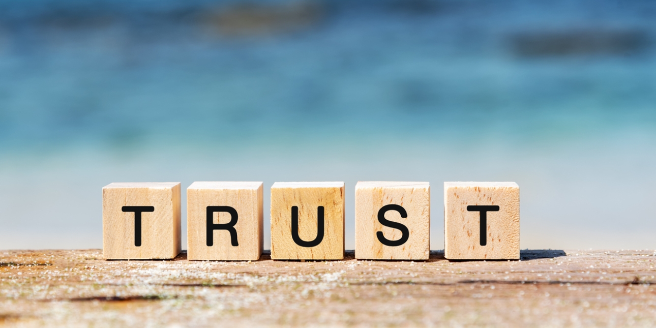 Five wooden blocks on a piece of wood spell out the word trust. The background is blue.
