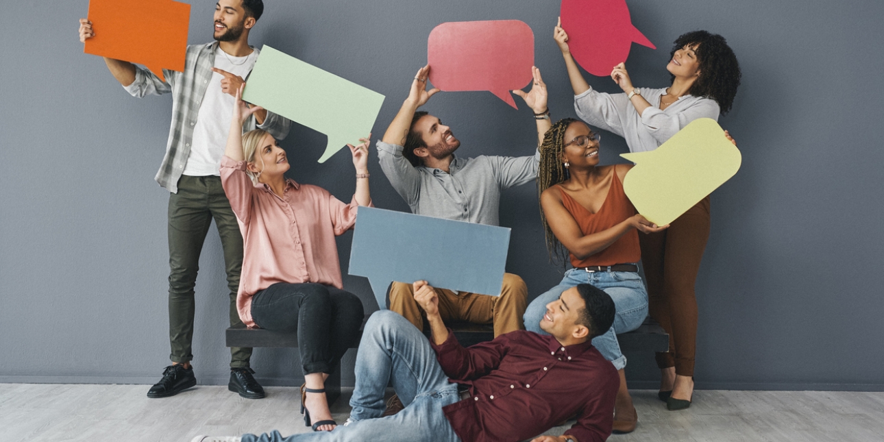 Six smiling men and women of different ethnicities hold up large speech bubbles cut from multicoloured card