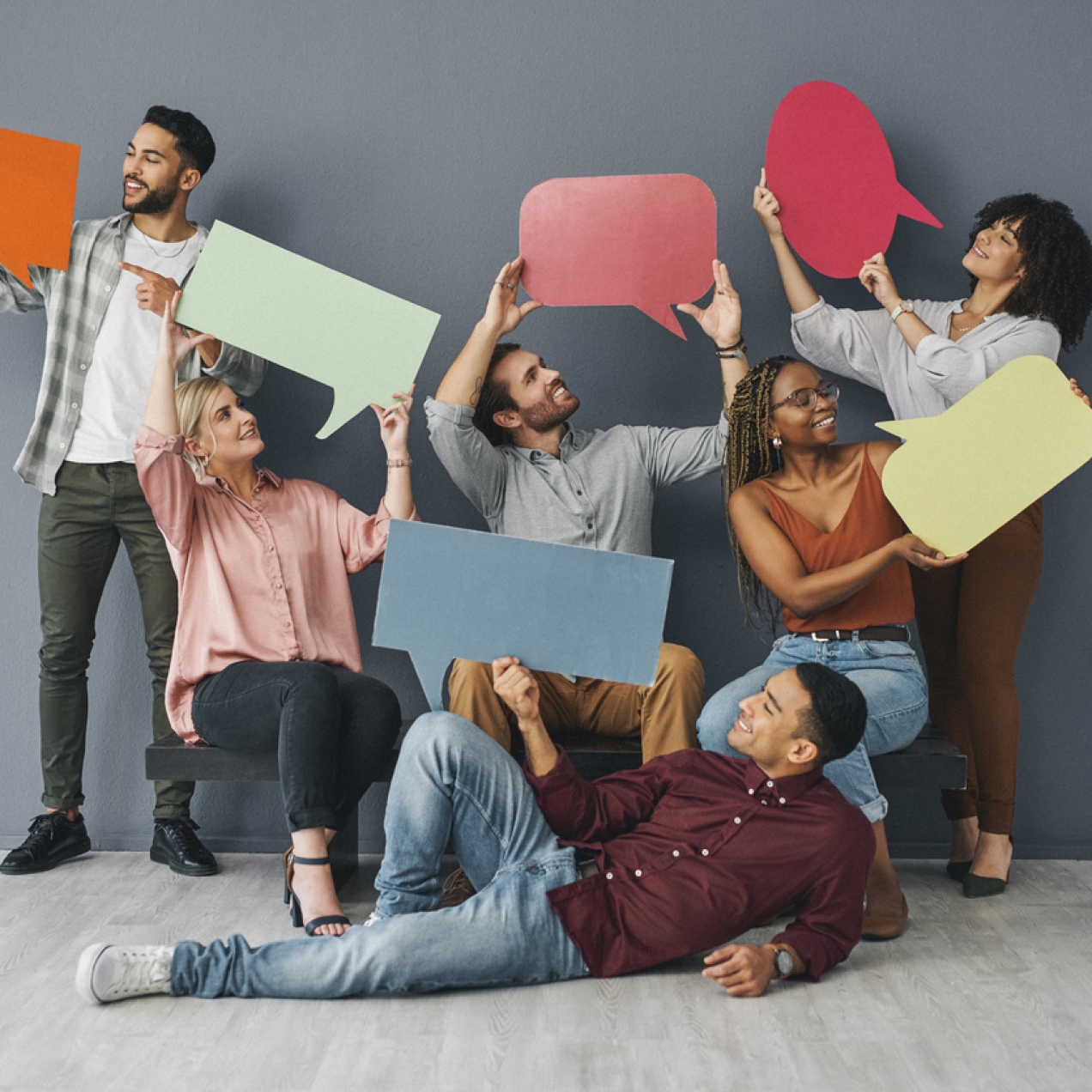 Six smiling men and women of different ethnicities hold up large speech bubbles cut from multicoloured card