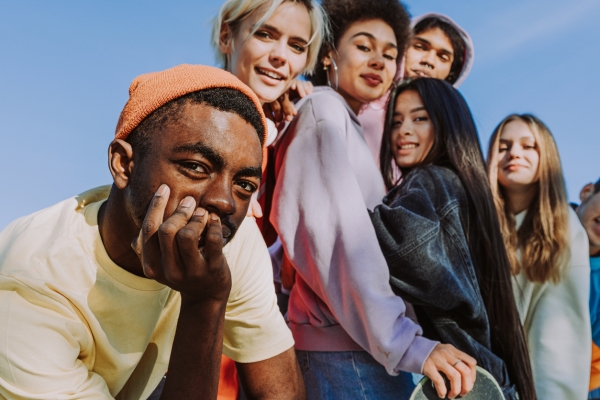 Group of six young people in casual clothes looking down to the camera. The sky is blue behind them.