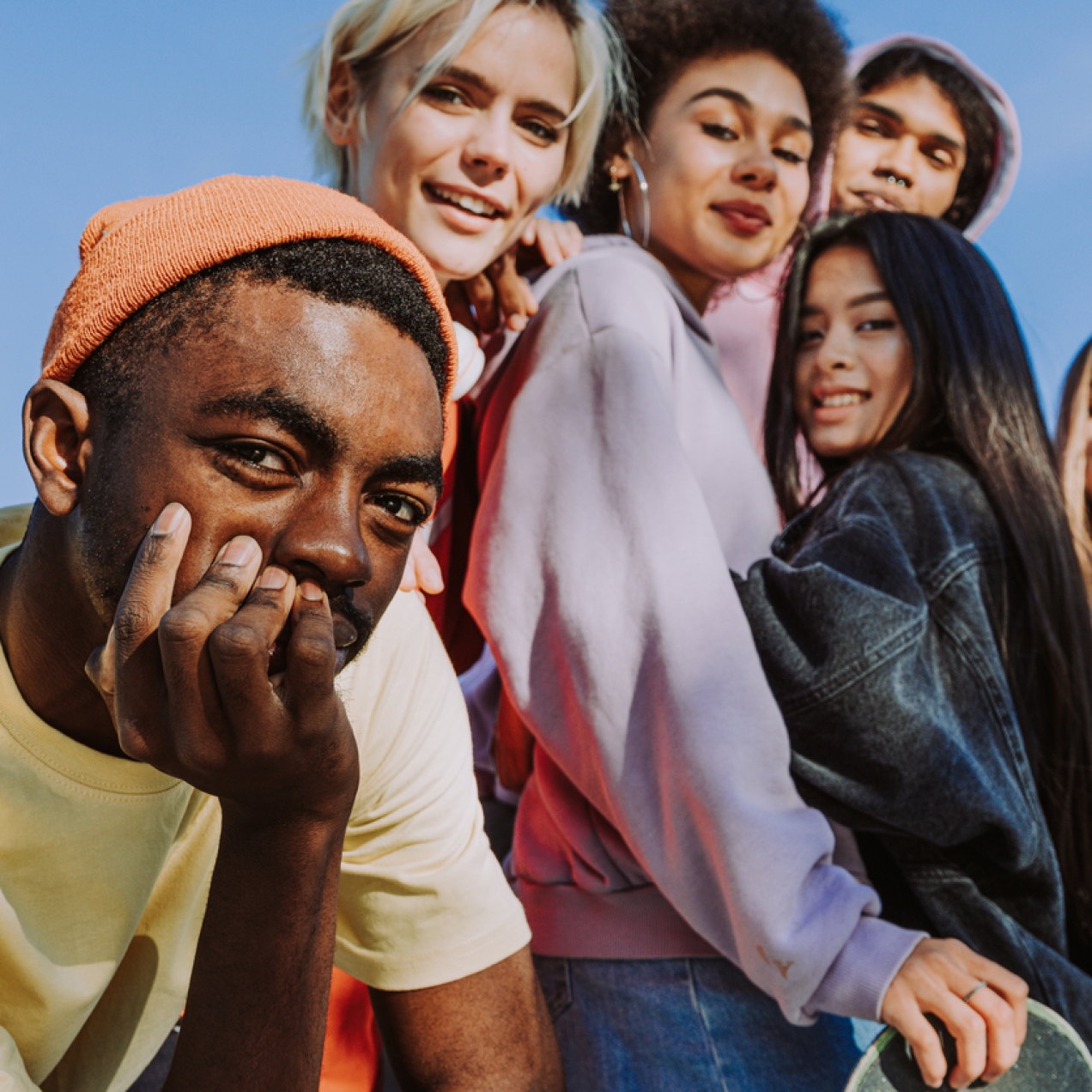 Group of six young people in casual clothes looking down to the camera. The sky is blue behind them.
