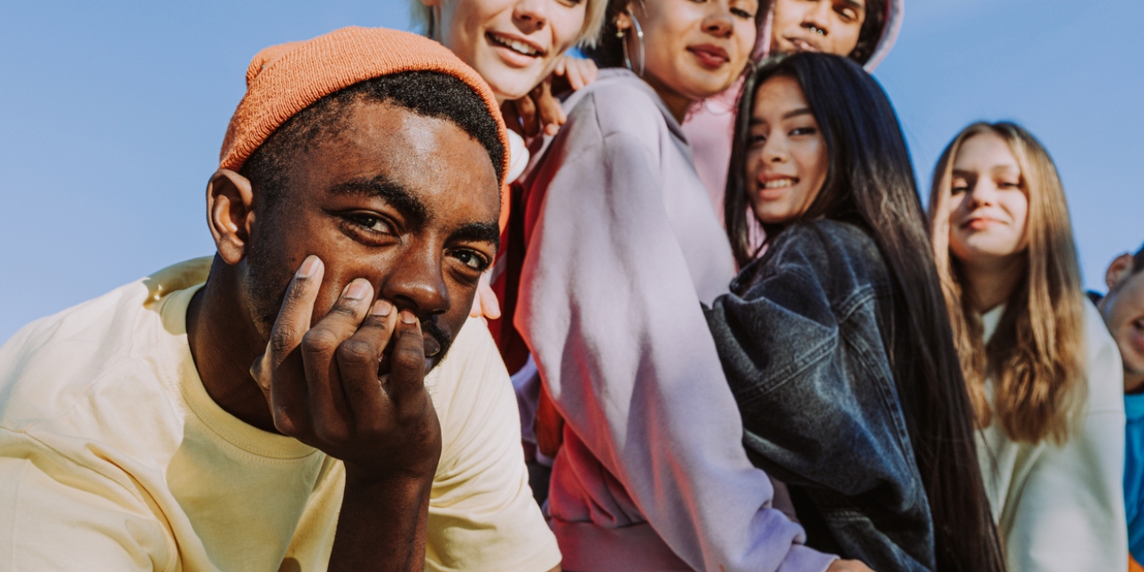 Group of six young people in casual clothes looking down to the camera. The sky is blue behind them.