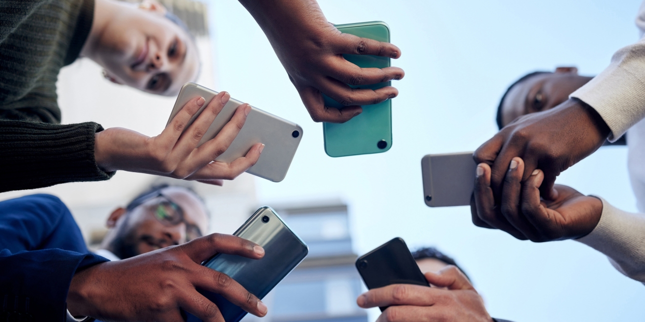 Photograph taken from the ground looking up at five people holding mobile phones in a circle