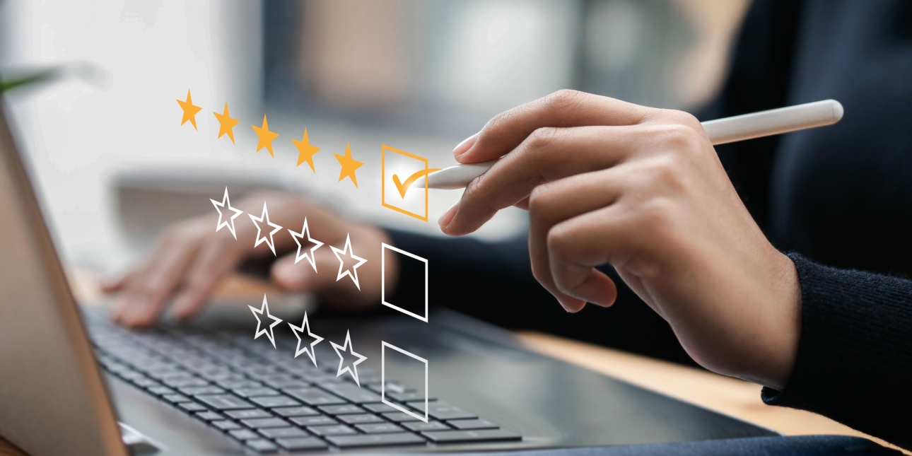 A hand holding a stylus is ticking a box next to five yellow stars. Below it are boxes with four and three white outlined stars. These stars are superimposed over a laptop keyboard