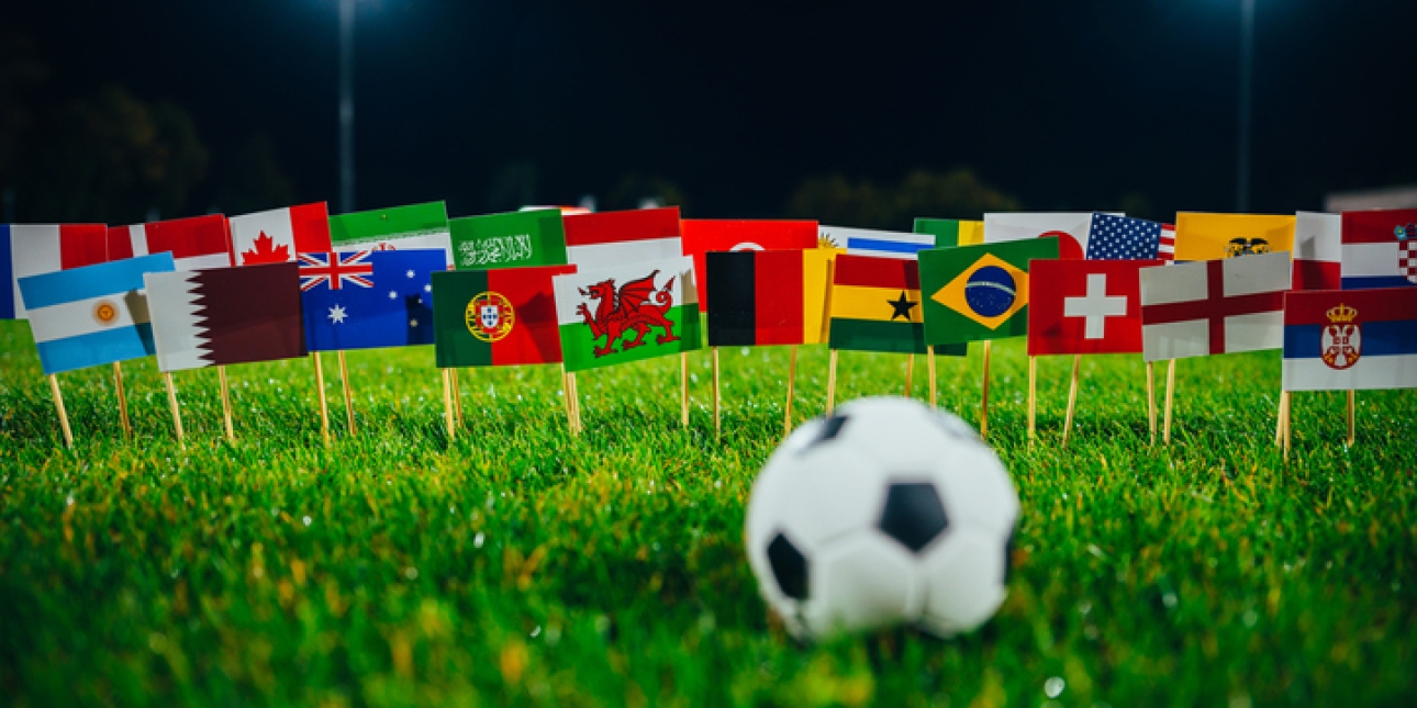 A football on grass. In the background are flags of the participating football team's countries.