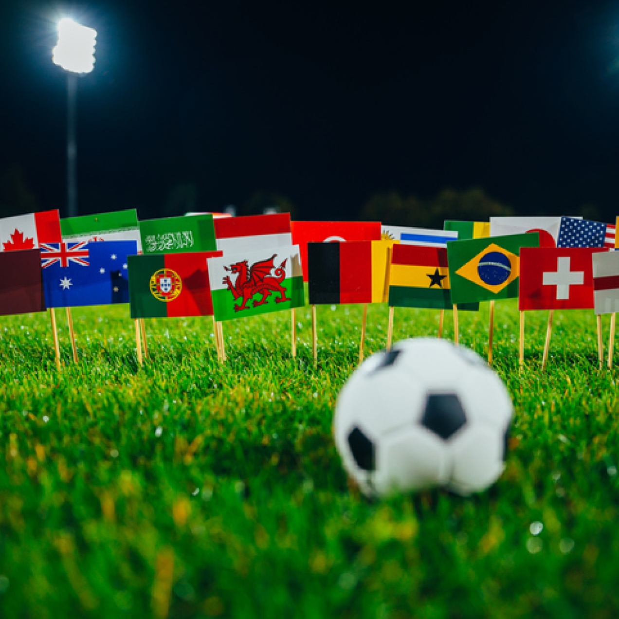 A football on grass. In the background are flags of the participating football team's countries.