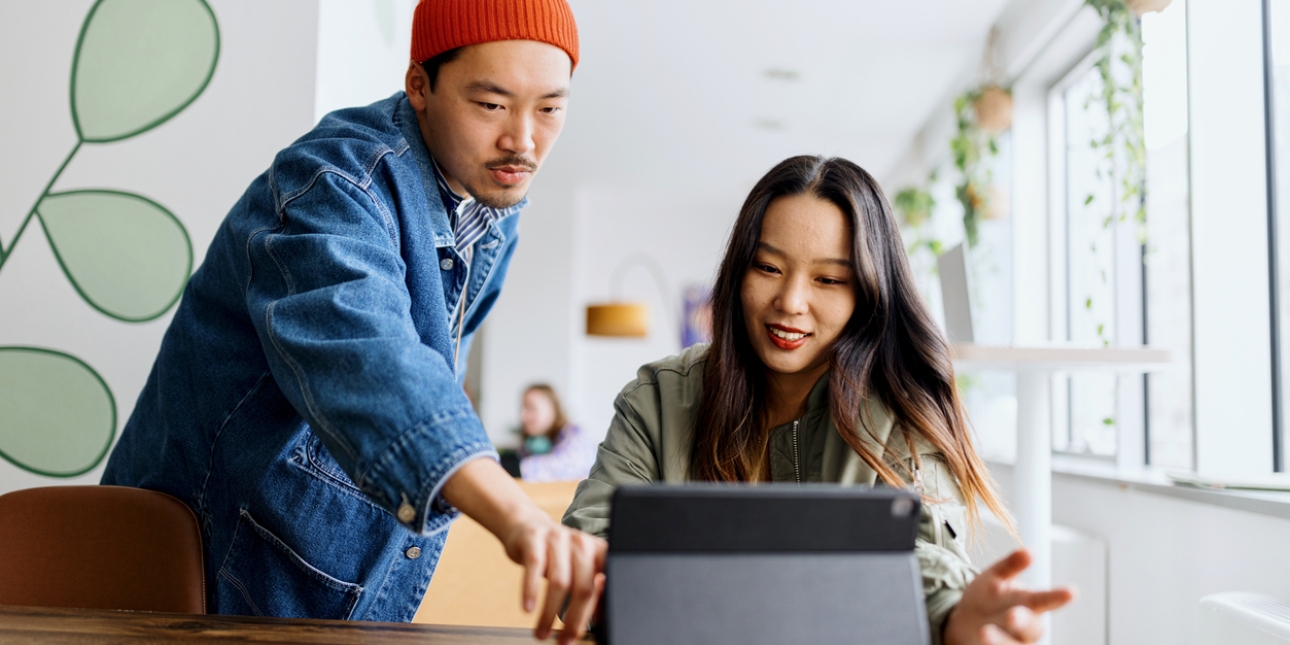 Two young colleagues discuss work over a tablet on a desk.