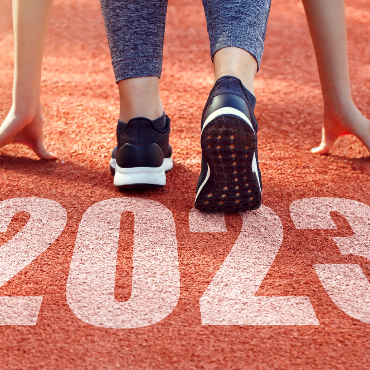 The back of a runner crouched down in the start position of a running track with 2023 written on the surface of the track