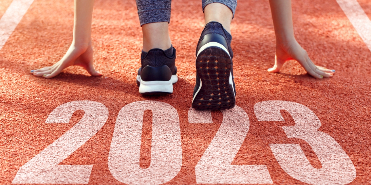 The back of a runner crouched down in the start position of a running track with 2023 written on the surface of the track
