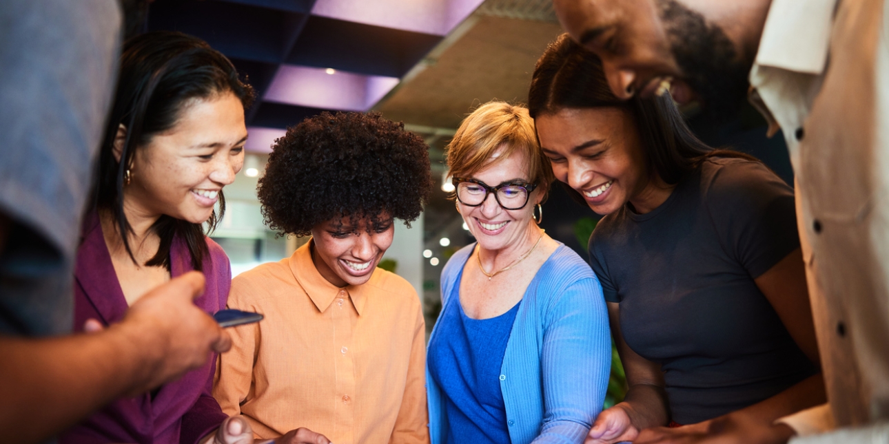 Four women and two men of different ethnicities look at each other's phones smiling at the screens