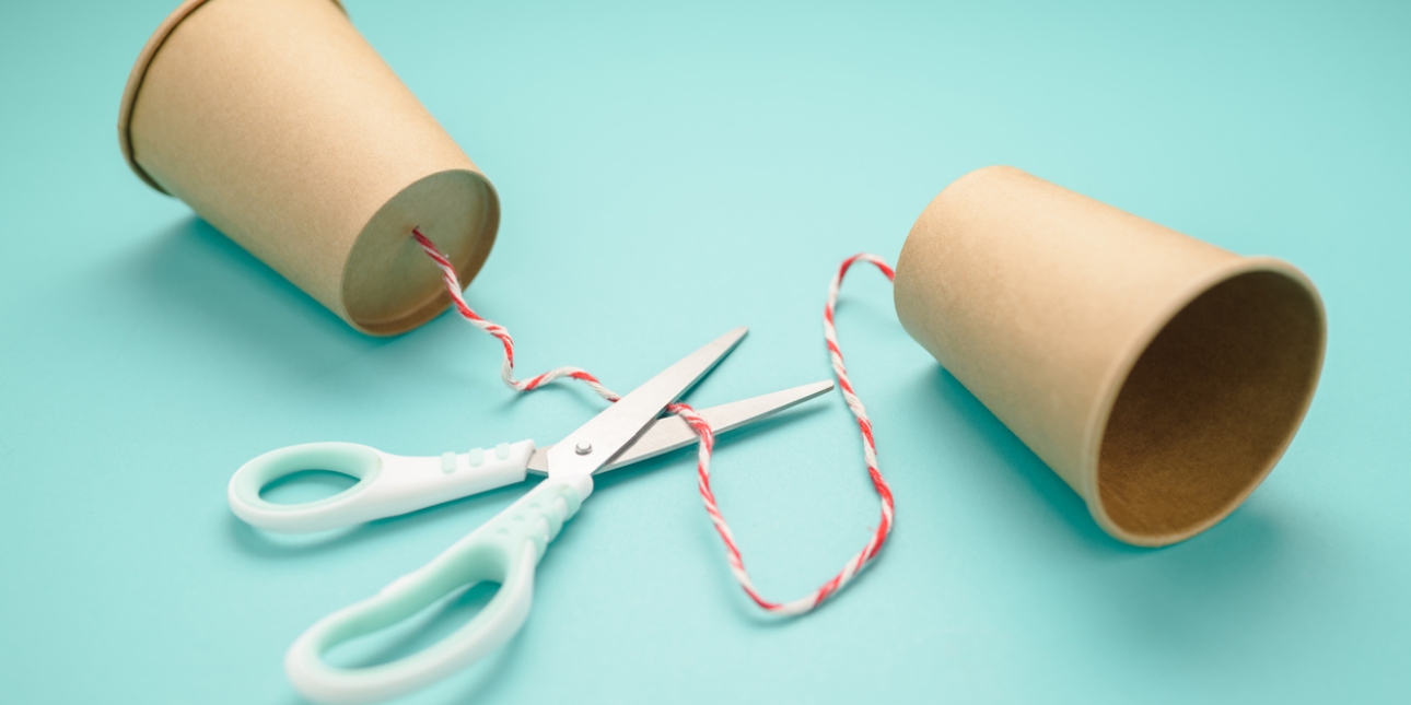 Two brown paper cups connected by string through a hole in the bottom of the cups. A pair of scissors is open and ready to cut the string.