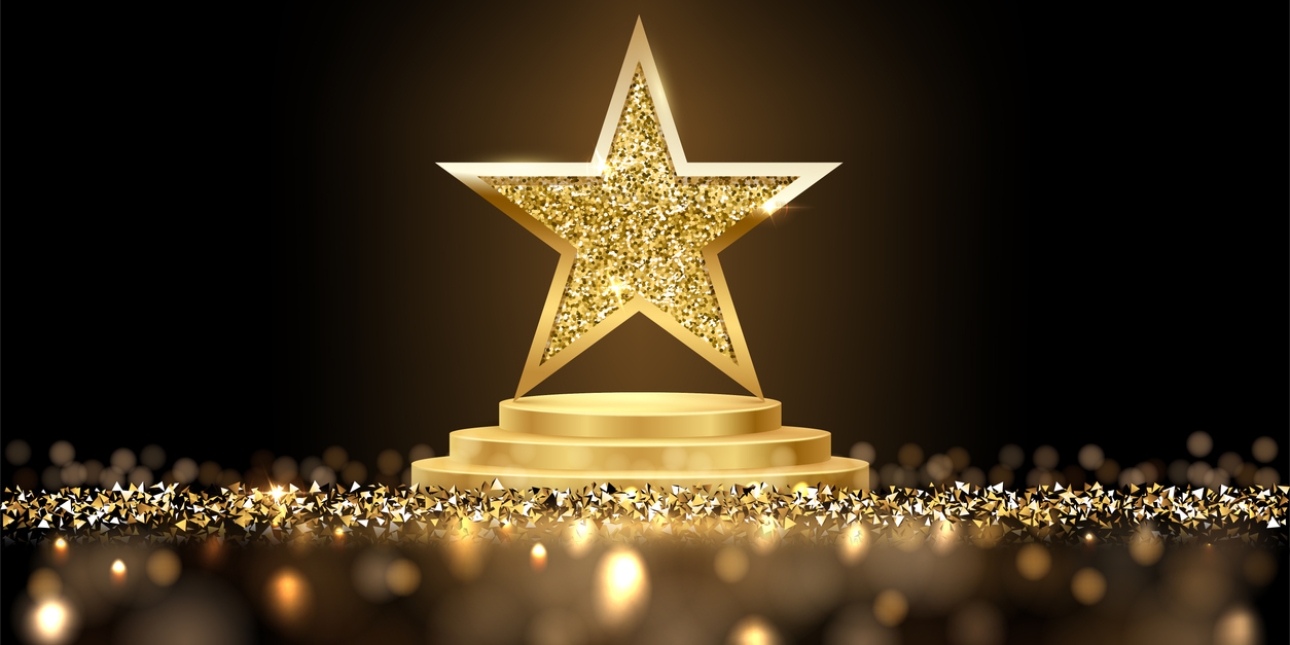Computer generated image of a three dimensional gold star on a gold circular podium. The centre of the star dazzles. There is a carpet of gold triangle shapes around the podium