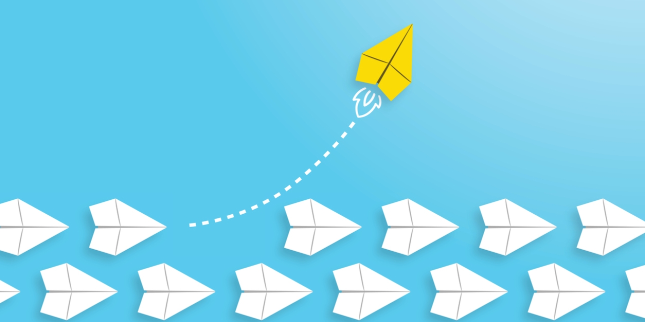 Illustration of more than a dozen white paper aeroplanes in three rows pointing to the lower right of the screen. Lifting off from the top row and heading towards the right and corner is a yellow rocket with smoke from its exhaust.