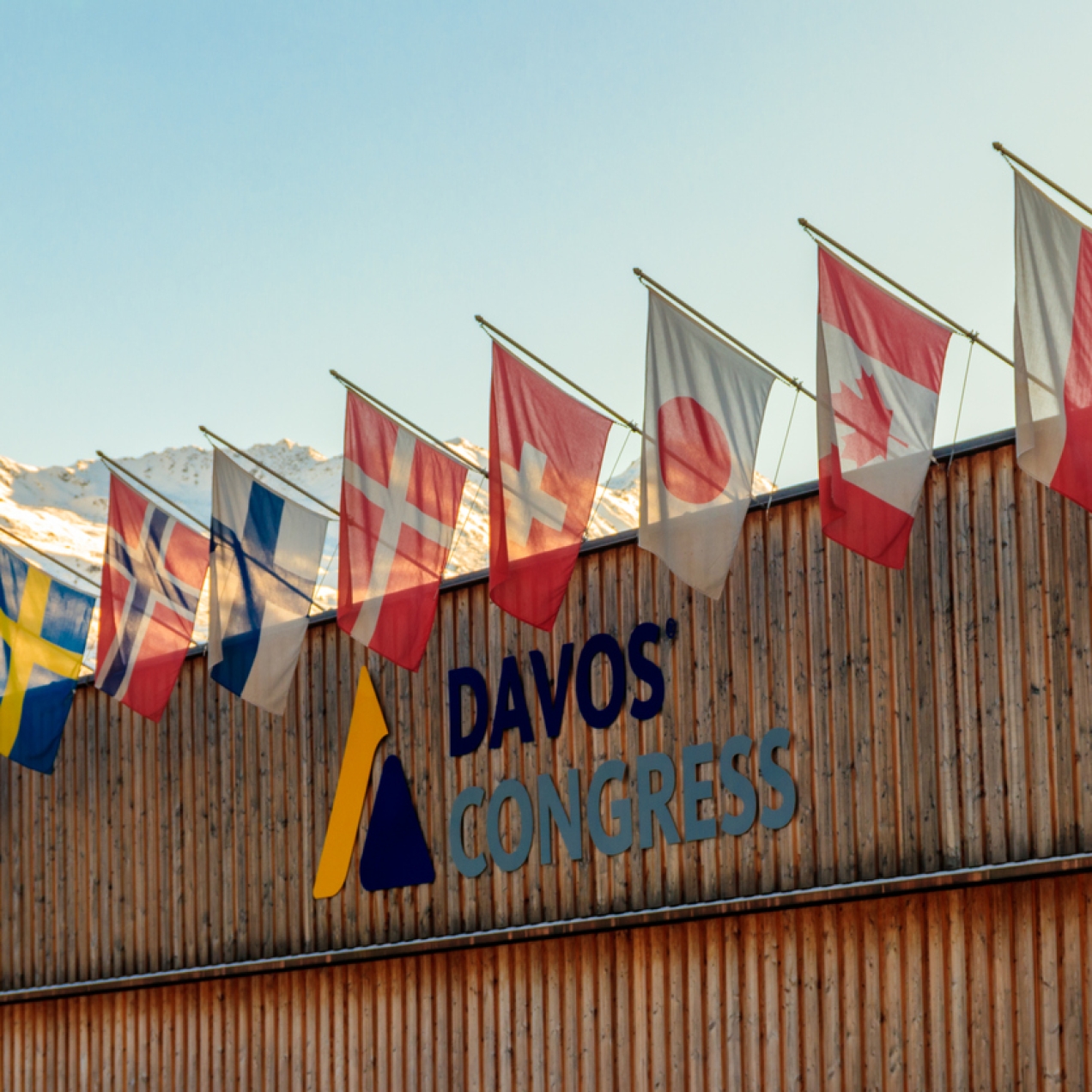 Close up exterior shot of Davos Congress Centre with flags displayed along it and snowy mountains in the background