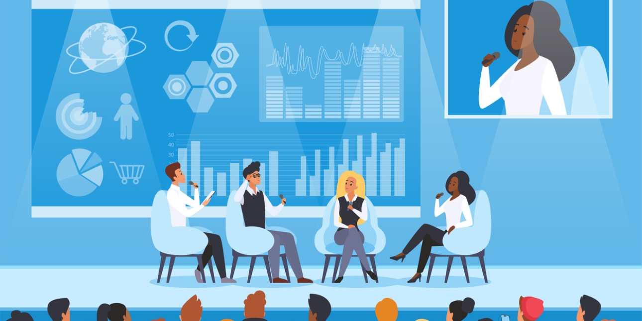 Four people of different ethnicities and gender sat on chairs on a conference stage in front of two rows of audience. Behind them is a screen with various graphics and an larger image of the current speaker, a Black woman in a white shirt, holding a