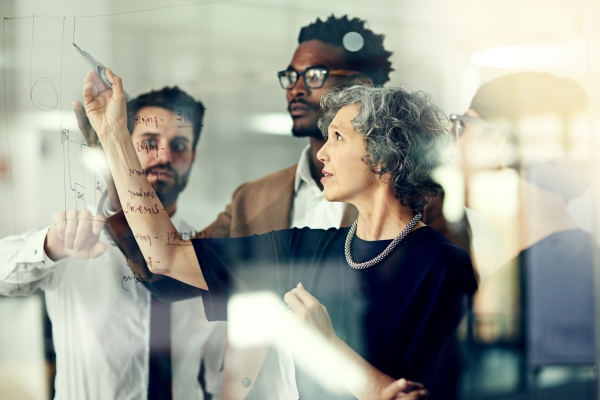 A business woman writes on glass with a marker while three male colleagues look on
