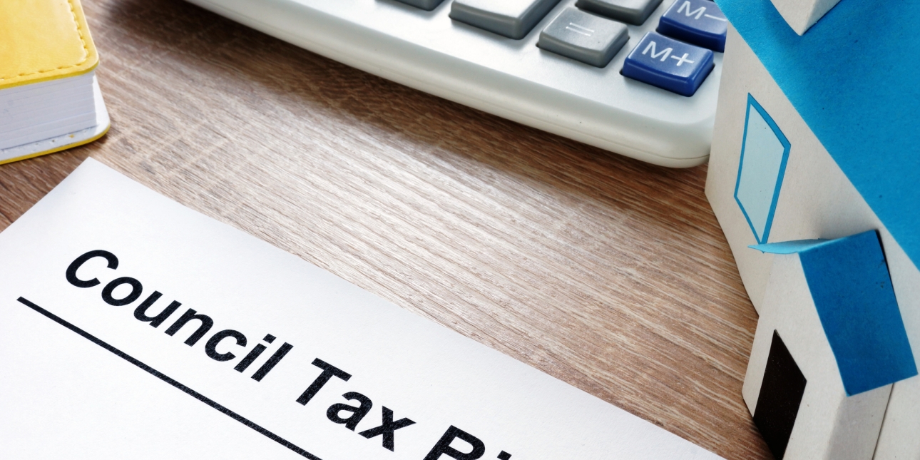 A council tax bill on a desk surrounded by a model of a detached house, a calculator and yellow notebook