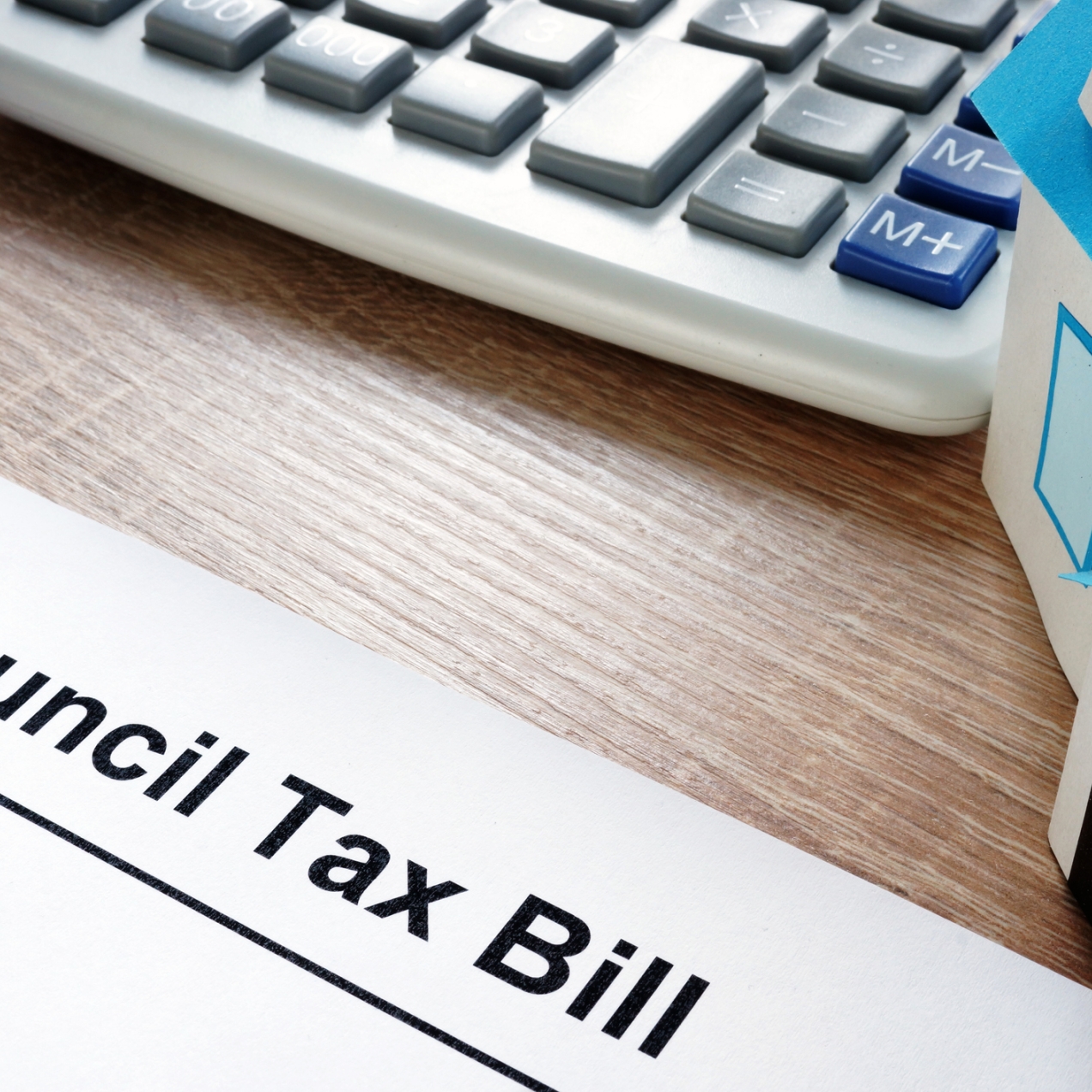 A council tax bill on a desk surrounded by a model of a detached house, a calculator and yellow notebook
