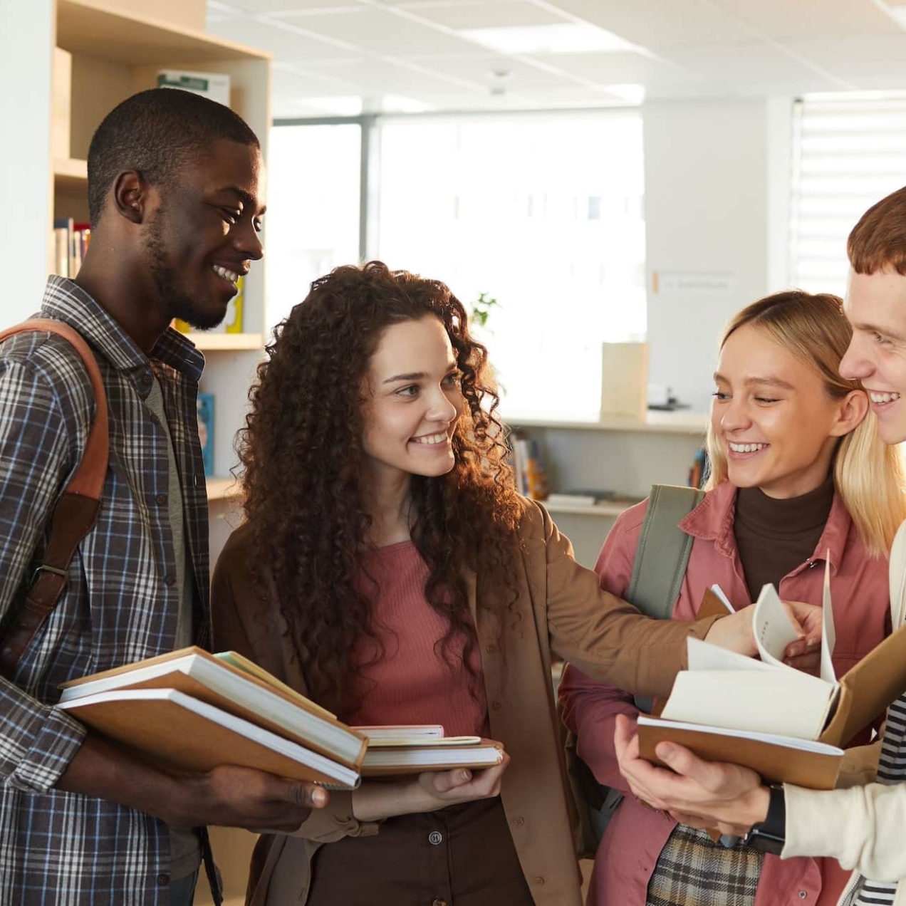 A group of four smiling university students stood gathered around a textbook