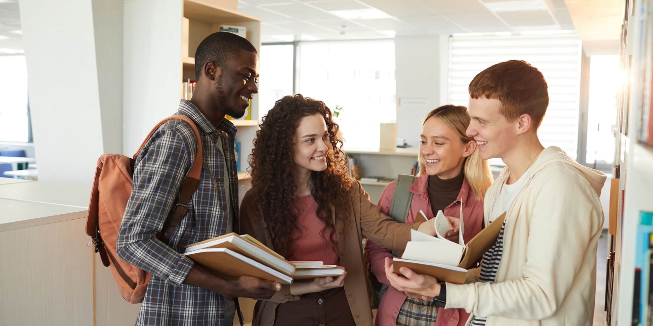 A group of four smiling university students stood gathered around a textbook