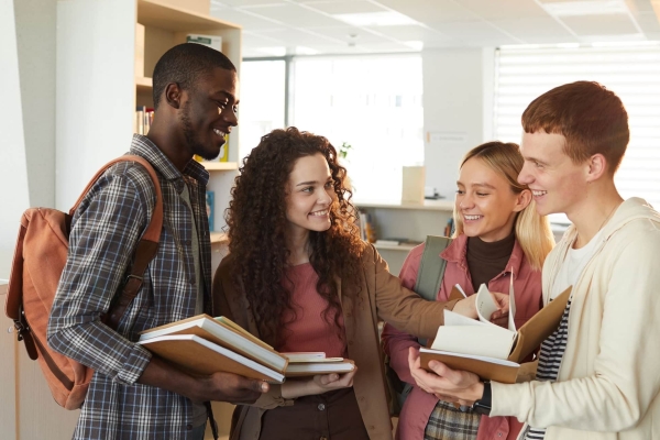 A group of four smiling university students stood gathered around a textbook