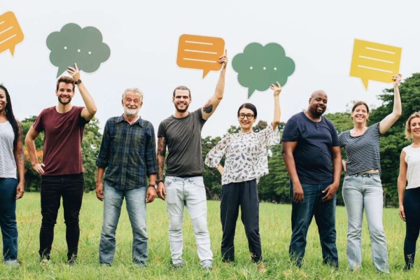 Eight people of different ages, genders and ethnicities stood on grass while holding cut out speech bubbles
