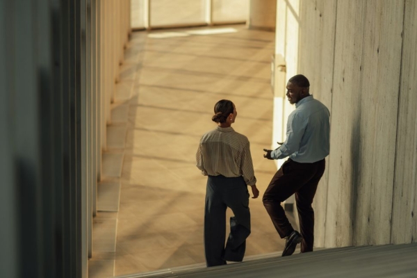 The backs of two business people having a conversation at the bottom of a staircase.