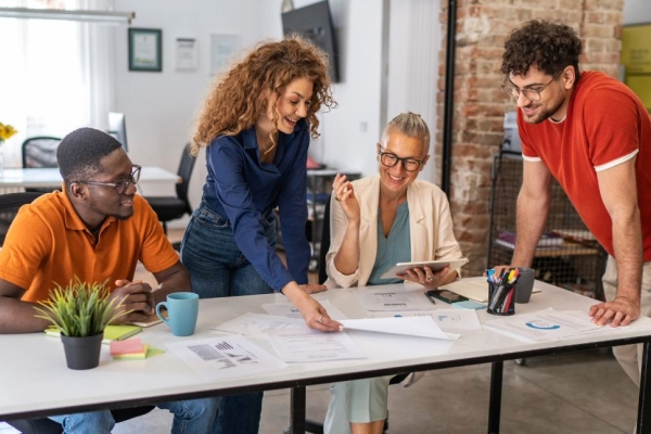 Four colleagues of different genders and ethnicities discuss paperwork on a table in a modern office.