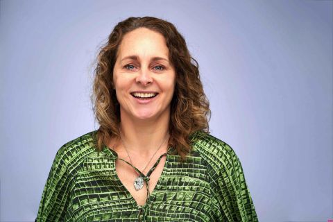 Headshot of Helen Ellis smiling at the camera wearing a green blouse in front of a grey backdrop
