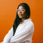 Adedoyin Jaiyesimi against an orange background. Adedoyin is a black woman with long hair and glasses who is wearing a white top.