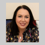 A portrait of Alison Gallagher-Hughes. Alison is a white woman with shoulder length dark hair and a floral blouse