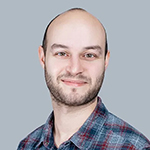 A colour portrait of Andrew White. Andrew is a white man with dark stubble, wearing a check shirt. The background is grey.