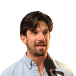 A colour portrait of Charlie Martin against a light grey background. Charlie is a white man with short dark hair wearing a grey shirt.