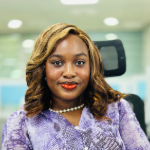 A colour portrait of Irene Ekong sat in a chair. Irene is a Black woman with shoulder-length brown-blond hair who is wearing a mauve top.
