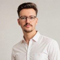 A portrait of James Sharp against a grey background. James is a white man with short dark hair and beard, who wears glasses and a white shirt