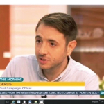 A screen shot of Jon Gerlis - a white man with brown hair who is wearing a light coloured shirt- on television.
