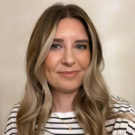 A colour portrait of Kat Trinder. Kat is a white woman with long light brown hair who wears a striped top.