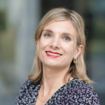 A colour photo of Lottie West. Lottie is a white woman with long blond hair, wearing a dark patterned top.