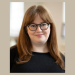 A portrait of Orla Graham. Orla is a white woman with long brown hair, glasses and a black top.