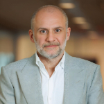 A colour portrait of Ronn Torossian. Ronn is a white man with receding hair, grey beard and grey suit jacket over a white collared shirt.