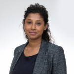 A colour portrait of Sinthu Satchi wearing a grey jacket over a black top.