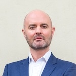 A colour portrait of Tim Toulmin. Tim is a white man with a short beard, wearing a navy blazer and white shirt.